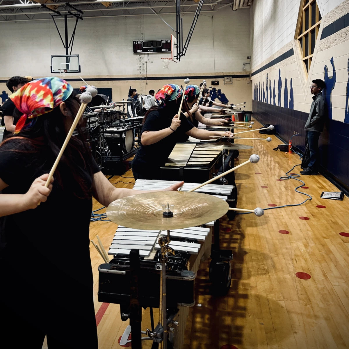 People playing drums in a gymnasium with colorful headscarves.