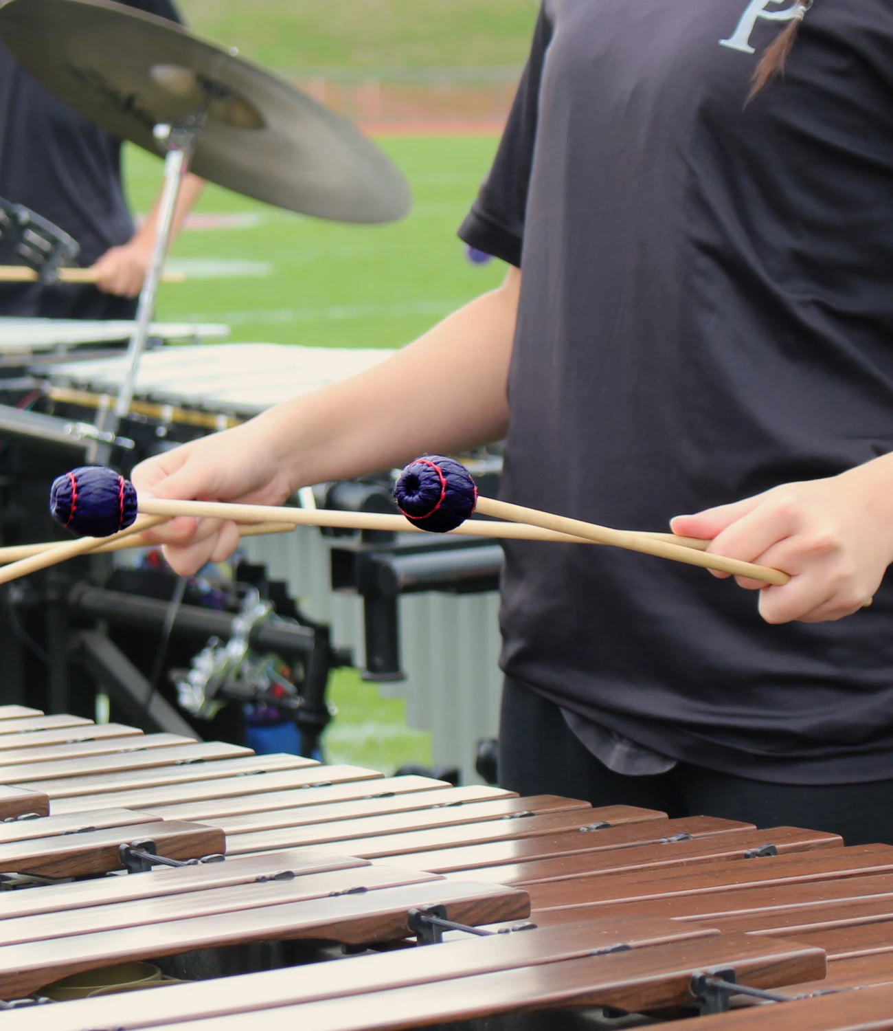 Person playing a marimba with mallets on a sports field background