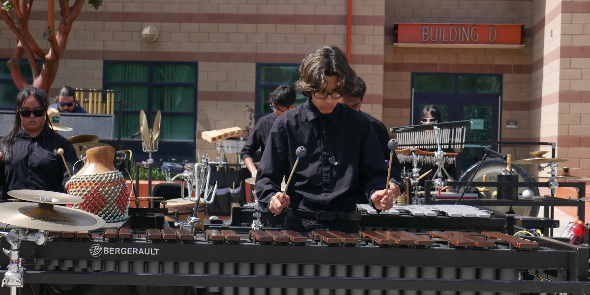 Person playing a marimba with a school building in the background