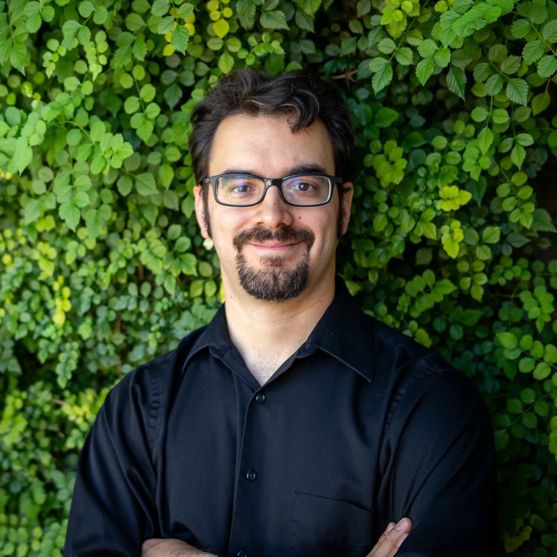 Man wearing glasses and a black shirt standing in front of a green leafy background