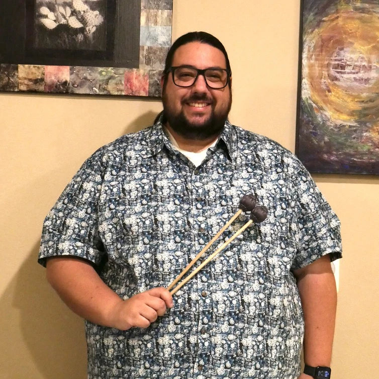 Man holding mallets in a room with framed artwork on the wall