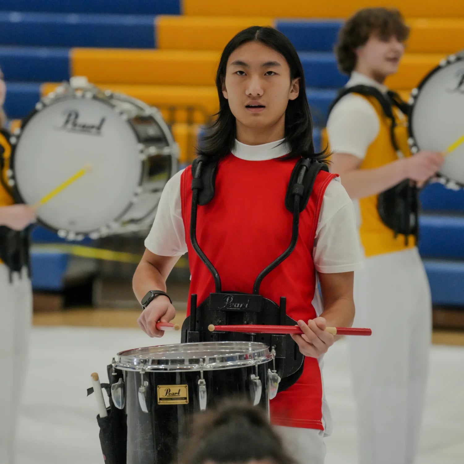 Person playing a drum with a red vest in a band setting